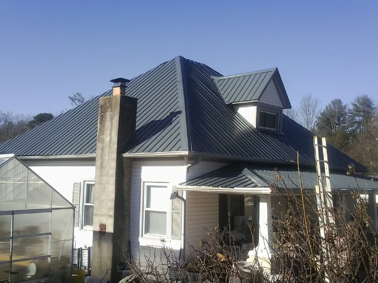 Dark blue standing seam metal roof on a white farmhouse with dormer — Slate & Tile Roof Repair by Roofing Brothers in Carman