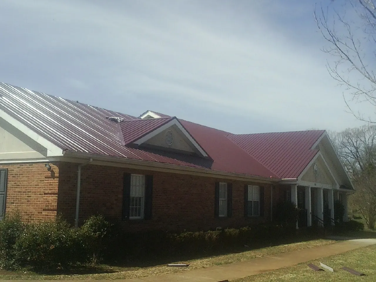 Red metal roof with gabled entries on a long brick building, from a Hail Damage Roof Repair job in Carman