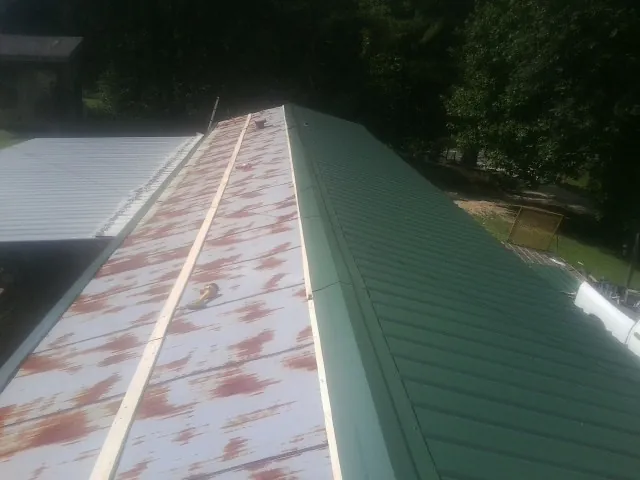 Old rusted panels beside newly installed green metal roofing — Wind Damage Roof Repair by Roofing Brothers in Carman