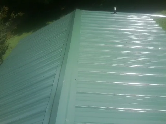 New green metal panels meeting at the ridge of a roof — Flat Roof Repair work by our crew in Carman
