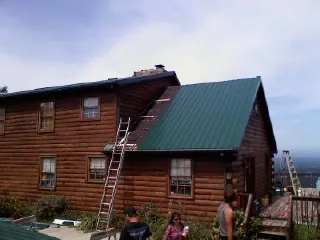 Green metal roof going on a two story log home with ladders set in Carman