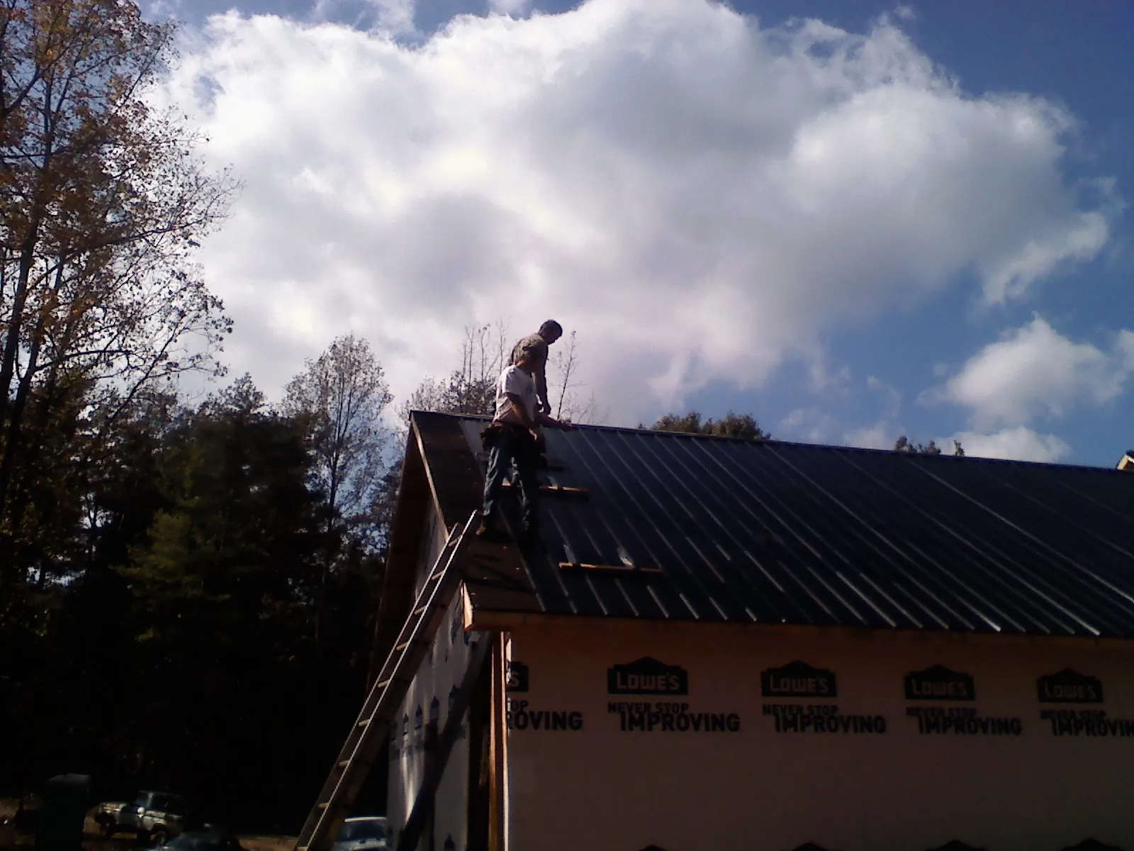 Roofer fastening dark metal panels high against a cloudy sky, from a Roof Inspection job in Carman
