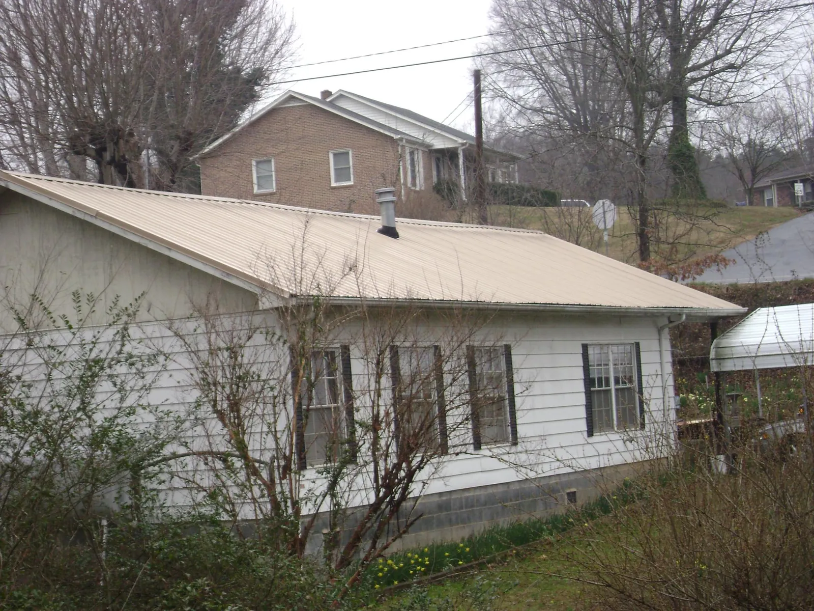 Tan metal roof on a white sided house set into a hillside — Commercial Roofing by Roofing Brothers in Carman