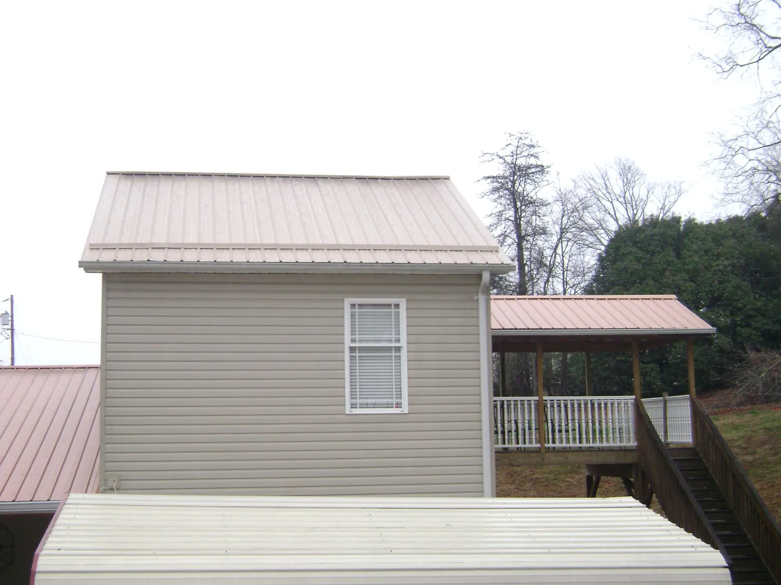 Tan metal roofs on a two story addition and attached porch, from a Roof Replacement job in Carman